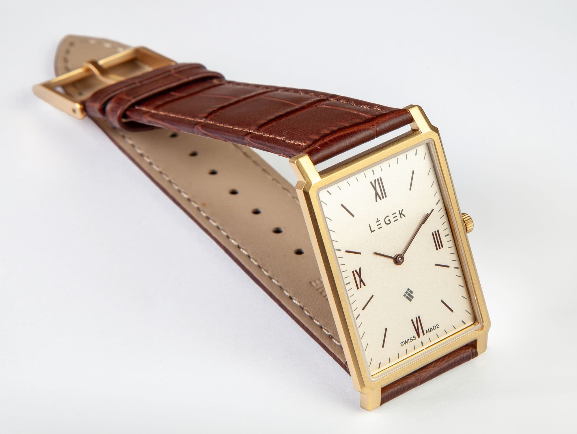 Product photography of a gold rectangular Swiss watch with a brown leather strap on a white background